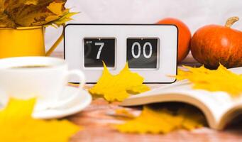 The flip clock shows 7 o'clock in the morning. Early awakening in autumn. A book and a cup of hot coffee in the foreground in blur. Close-up. photo
