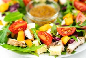 Healthy salad from chicken, tomatoes, cheese and arugula leaves with honey mustard sauce. Close-up. Selective focus. photo