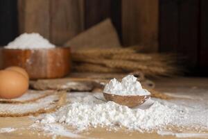 White wheat flour in a wooden spoon with barley ears Rice grains and eggs natural agricultural food on a dark wooden background photo
