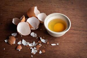 Broken egg shells and eggs on tray and pot, raw egg in small bowl at wooden background menu and recipe photo