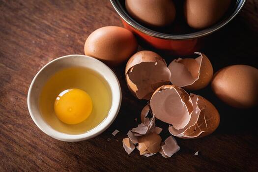 Broken egg shells and eggs on tray and pot, raw egg in small bowl at wooden background menu and recipe photo