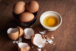 Broken egg shells and eggs on tray and pot, raw egg in small bowl at wooden background menu and recipe photo