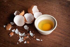 Broken egg shells and eggs on tray and pot, raw egg in small bowl at wooden background menu and recipe photo