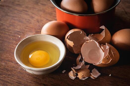 Broken egg shells and eggs on tray and pot, raw egg in small bowl at wooden background menu and recipe photo