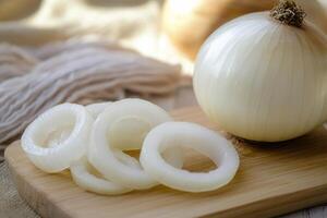 Freshly sliced white onions on a wooden cutting board with a whole onion and kitchen cloth in a sunlit kitchen setting photo