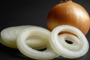 Freshly sliced onion rings next to a whole onion on a dark background showcasing their texture and color variations photo