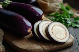 Freshly sliced eggplant on a rustic wooden cutting board with whole eggplants and herbs nearby photo