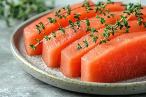 Fresh watermelon slices garnished with thyme on a patterned plate arranged on a textured surface photo