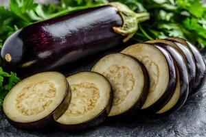 Freshly sliced eggplant surrounded by vibrant green herbs on a dark countertop photo