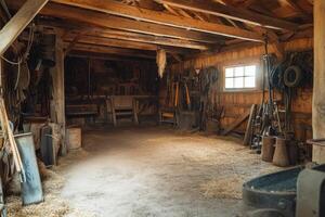 A rustic barn interior showcasing wooden beams, tools, and hay scattered across the floor in a tranquil rural setting during daylight photo