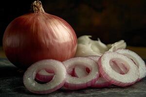 Fresh red onion and garlic cloves arranged artfully on a dark surface with sliced rings of onion showcasing vibrant colors photo