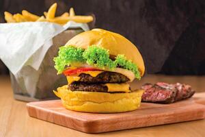 Double Beef Cheeseburger with Lettuce, Jalapeno, Tomato, Cheese, Steak Slices isolated on wooden board with french fries basket side view of fastfood photo