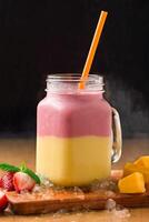 Mango Strawberry Layered Smoothie served in jar isolated on wooden board closeup side view of healthy drink photo