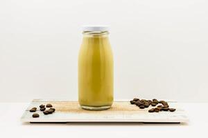 Cold Cafe Latte with Coffee Beans served in a Glass Bottle isolated on wooden board side view of cold beverage on white background photo