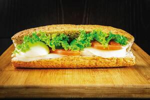 Egg Veggie Diet Sandwich with Cheese, Onion, Lettuce, and Tomato isolated on wooden board side view of breakfast on dark background photo