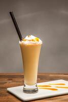 Salted Caramel Mango Milkshake with Whipped Cream and Drizzle served in glass isolated on wooden table side view of cold beverages drink photo