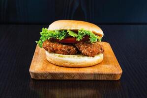 Crispy Chicken Fillet Burger with Lettuce, Tomato and Cheese isolated on wooden board side view of fastfood on dark background photo