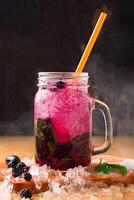 Blackberry Mojito with Mint and Lime served in jar with straw isolated on wooden board side view of perfect drink for a hot summer day photo