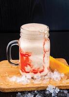 Mango Lassi with Strawberry Drizzle served in jar isolated on wooden board closeup side view of healthy drink photo