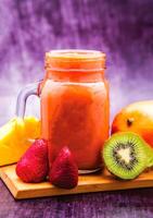 Tropical Fruit Smoothie with Mango, Strawberry, Kiwi and pineapple served in mug isolated on wooden board closeup side view of antioxidant juice photo