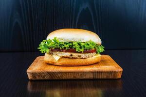 Classic chicken Cheeseburger with Lettuce, Tomato, and Cheese isolated on wooden board side view of fastfood on dark background photo
