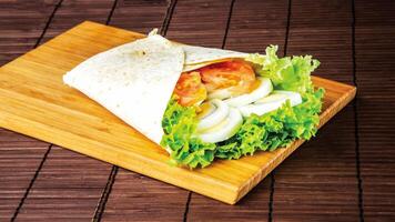 Boiled Egg Wrap Shawarma with Lettuce and Tomato isolated on wooden board closeup side view of fast food on dark background photo