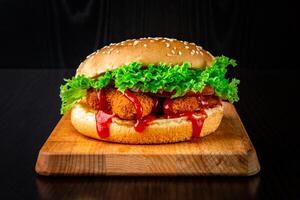 Crispy Chicken Nuggets Burger with Lettuce, Tomato and Ketchup isolated on wooden board side view of fastfood on dark background photo