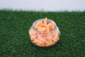 Crispy Corn Puffs in a jar on grass. Selective focus photo