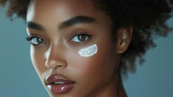 Vibrant commercial close-up of a young Black woman with glowing skin, gently applying a layer of cream to her cheek, with a soft gray backdrop that highlights her complexion, perfect for beauty photo