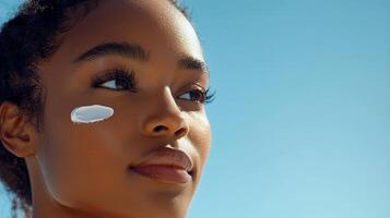 In a bright, minimalist setting, a close-up of a Black woman with dark brown hair and clear skin, carefully applying cream to her face, her calm expression enhancing the appeal of the skincare photo