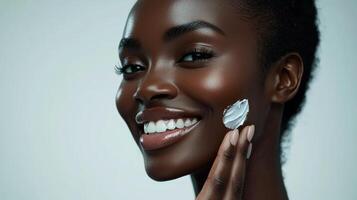 Advertisement image of a Black woman with flawless skin, softly smiling as she applies a moisturizing cream to her cheek with her fingertips, set against a clean, neutral gray background, perfect photo