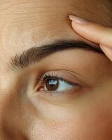 Close-up of a woman's forehead with deep wrinkles, as she uses her fingers to pull and stretch the skin, highlighting the effects of aging and skin elasticity loss, her dark brown hair pulled photo