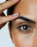 Extreme close-up of a woman's forehead, showing deep wrinkles as she pulls the skin apart with her fingers, emphasizing signs of aging and reduced skin elasticity, her dark hair slightly pulled photo