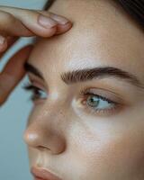 Extreme close-up of a woman's forehead, showing deep wrinkles as she pulls the skin apart with her fingers, emphasizing signs of aging and reduced skin elasticity, her dark hair slightly pulled photo