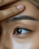 Extreme close-up of an Asian woman's forehead, showing deep wrinkles as she pulls the skin apart with her fingers, emphasizing signs of aging and reduced skin elasticity, her dark hair slightly photo