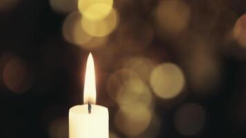 A single candle is lit in front of a blurry background video