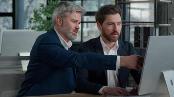 Mature businessman mentoring man discussing project on computer consulting investor client about digital investment in office Caucasian businessmen colleagues working together discuss data management video