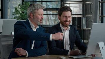 Happy Caucasian men businessmen business partners discussing financial growth looking at computer screen in office smiling colleagues males entrepreneurs discuss plan project strategy working together video
