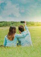 Young happy couple taking a selfie sitting in the field. Couple in love taking a selfie sitting in a beautiful field photo