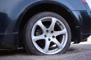 Car flat tire. Close up of flat rear tire of black sedan car vehicle automobile punctured by nail. Concept of failure, breakdown, stuck, being late because of car flat tire. photo