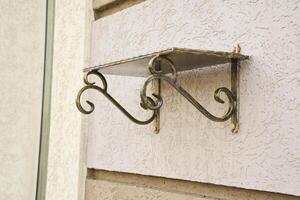 Forged Brackets with a memorial shelve for flowers. Bronze forged shelf with beautiful holders with scrolls and ornaments on the facade of a building. photo