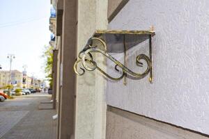 Forged Brackets with a memorial shelve for flowers. Bronze forged shelf with beautiful holders with scrolls and ornaments on the facade of a building. photo