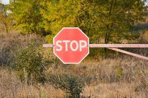 Old road sign stop on the barrier. Rumpled road sign on a greenery background. Stop sign in the field. Rural suburb Background photo