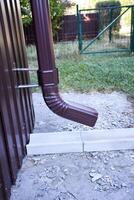 A close-up of a brown gutter pipe. The installation that drains water from the roof. Drainage system attached to the house. Guttering system. photo