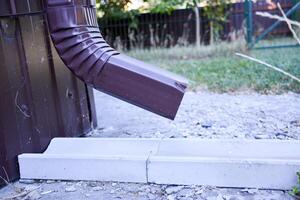 A close-up of a brown gutter pipe. The installation that drains water from the roof. Drainage system attached to the house. Guttering system. photo