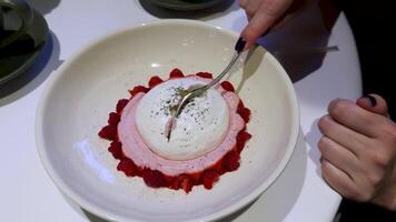 A close-up of a beautifully presented dessert with whipped cream and fresh raspberries in a white ceramic bowl. The dish is being enjoyed with a spoon, highlighting its delicate texture and vibrant video