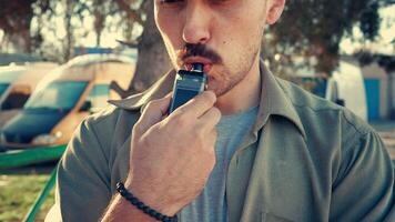 Young man enjoys vaping outdoors during sunset while relaxing in a serene environment video