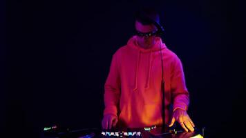 DJ performs live set with vibrant lighting in a dark studio, showcasing electronic music skills and engaging the audience video