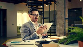 Professional man reviewing documents on a tablet in a modern office space during the day video