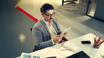 Young professional analyzing data on a tablet while seated at a modern office desk during daylight hours video